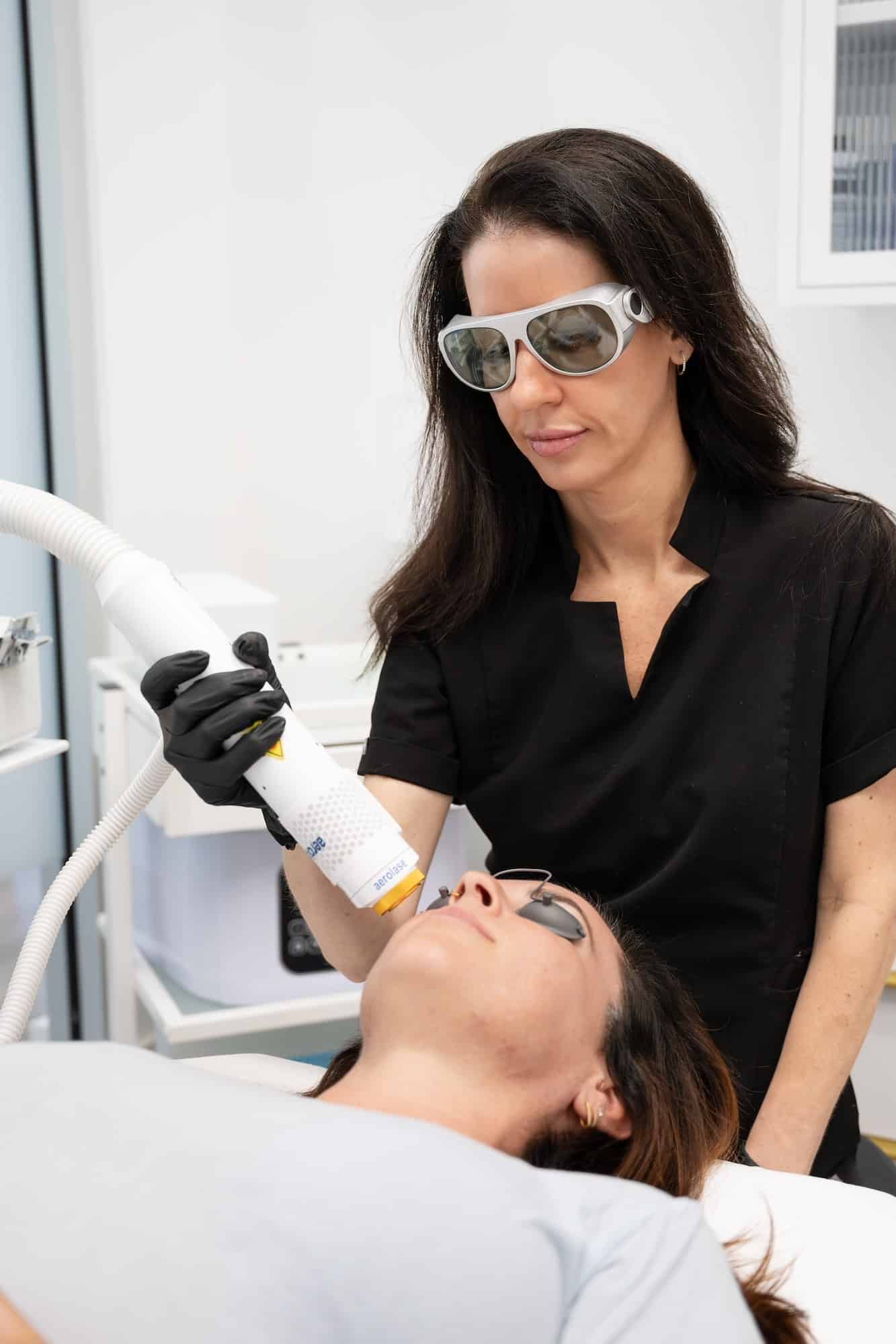 Provider performing erbium laser treatment on patient’s face while wearing protective eyewear in a clinical setting - SG Aesthetics & Wellness Provider performing erbium laser treatment on patient’s face while wearing protective eyewear in a clinical setting